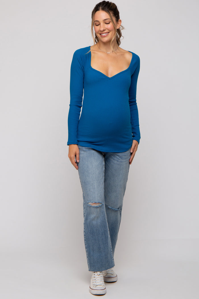 woman wearing a blue long sleeve maternity top with a sweetheart neckline and a baby bump, paired with distressed light jeans
