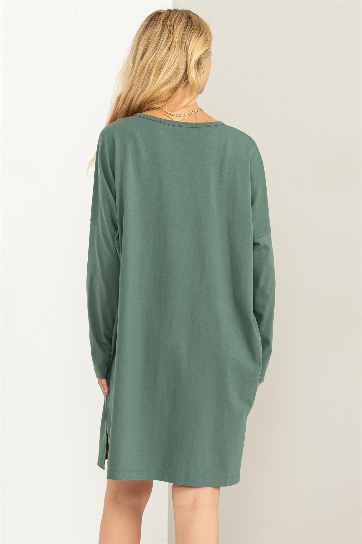 woman wearing a green long sleeve oversized dress with side slits, viewed from the back