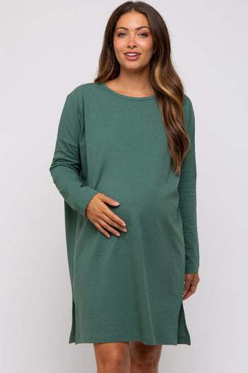woman wearing a green long sleeve maternity dress and gently holding her baby bump