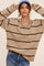 woman wearing a beige striped sweater with black stripes and a blue cap, accessorized with layered gold necklaces and denim jeans