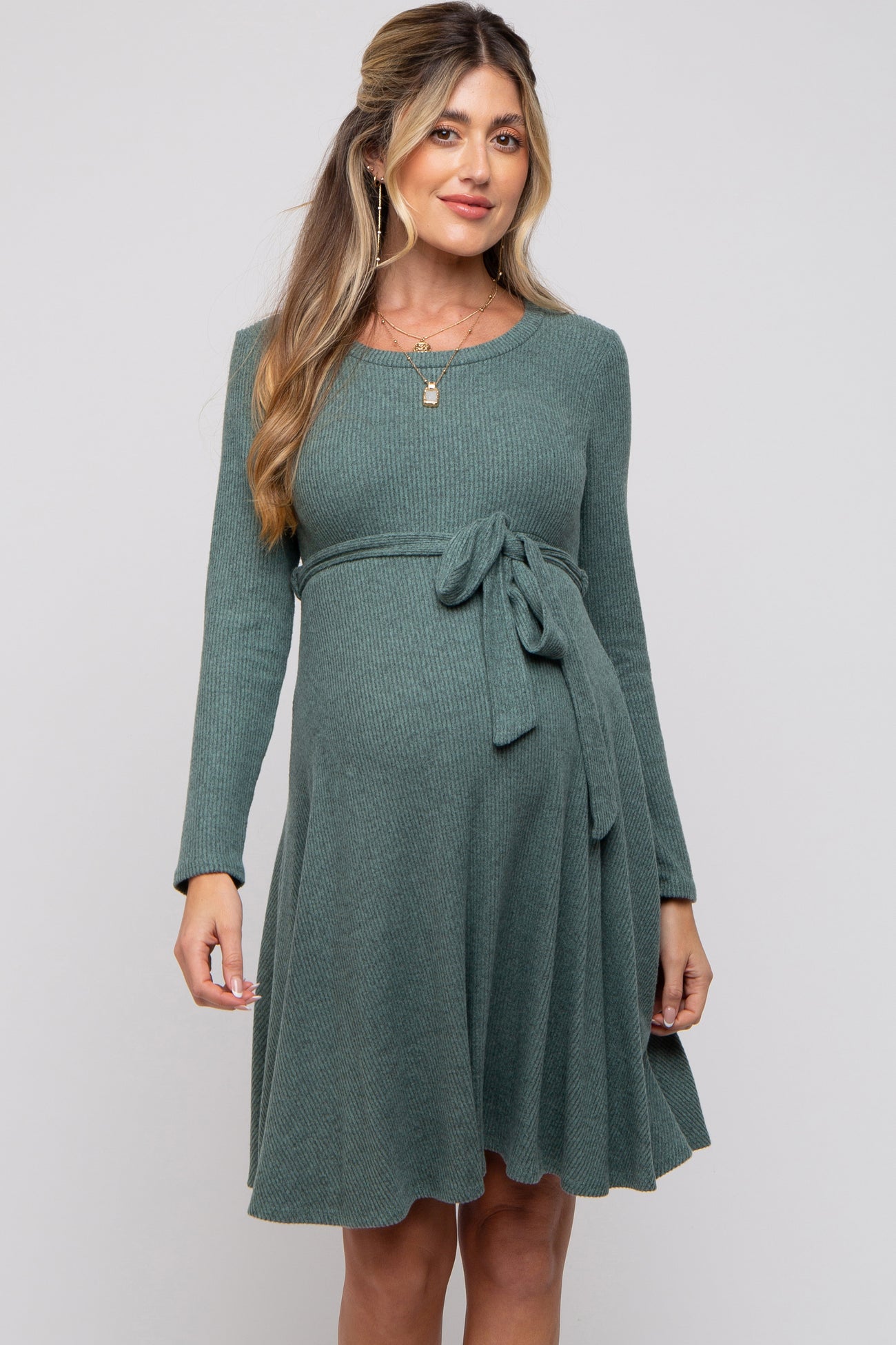 woman wearing a green long sleeve knitted maternity dress with a tie waist and a visible baby bump
