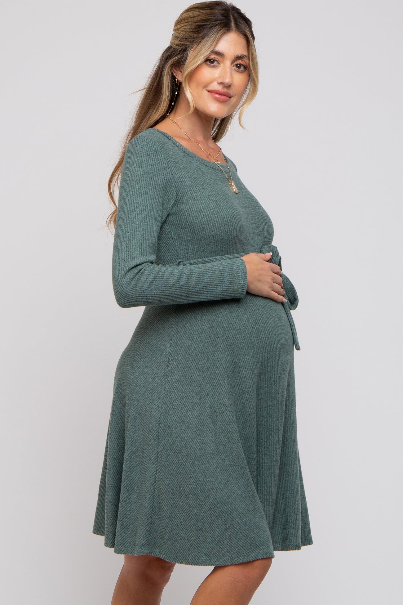 woman wearing a green ribbed maternity dress with long sleeves and a tie waist, highlighting her baby bump