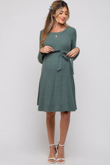 woman wearing a teal long sleeve maternity dress with a tie waist and a visible baby bump