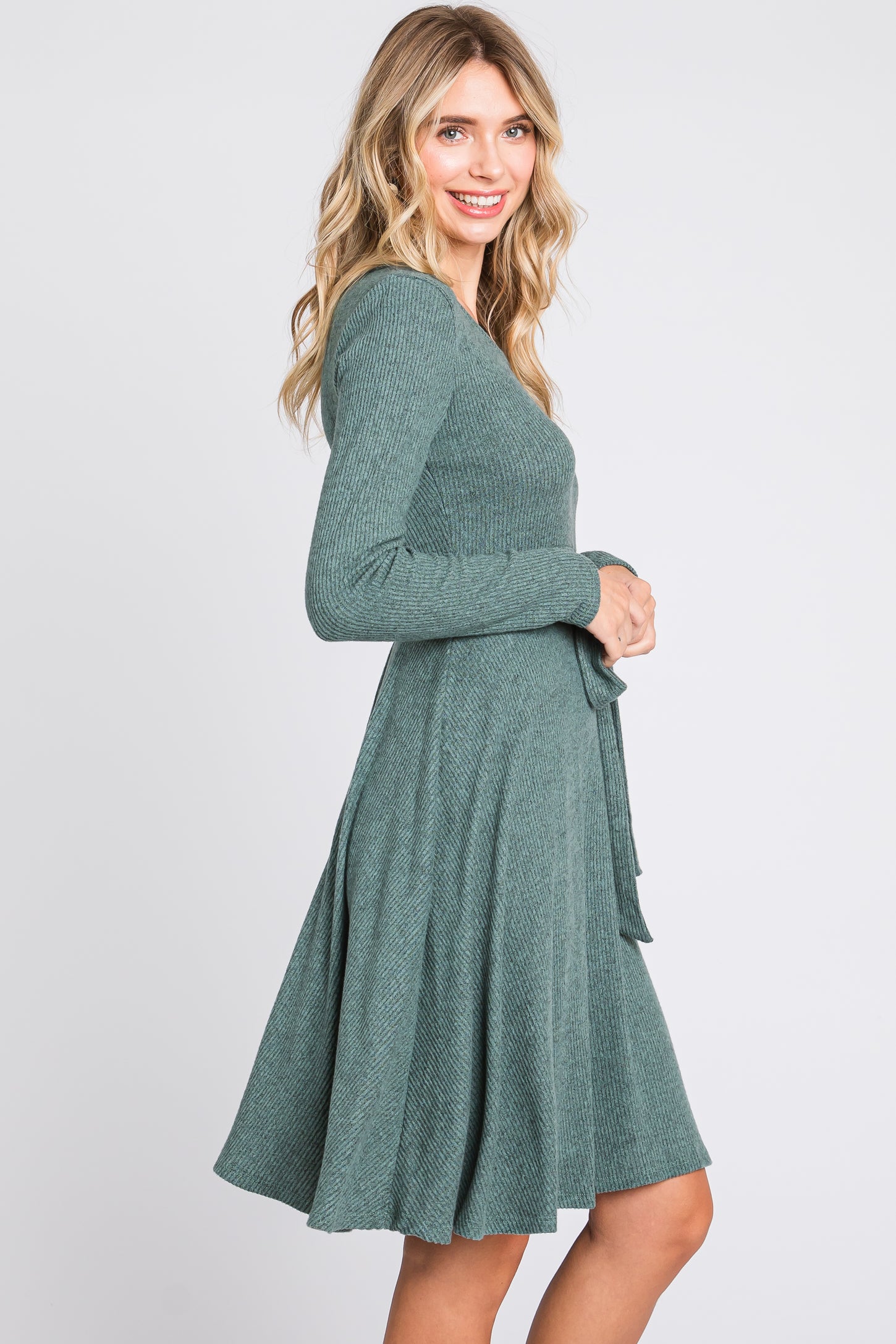 woman wearing a green long sleeve fit and flare dress with a tie waist and flared skirt