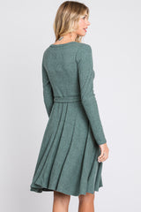 woman wearing a green ribbed long sleeve dress with a flared skirt and a tied waist detail, viewed from the back