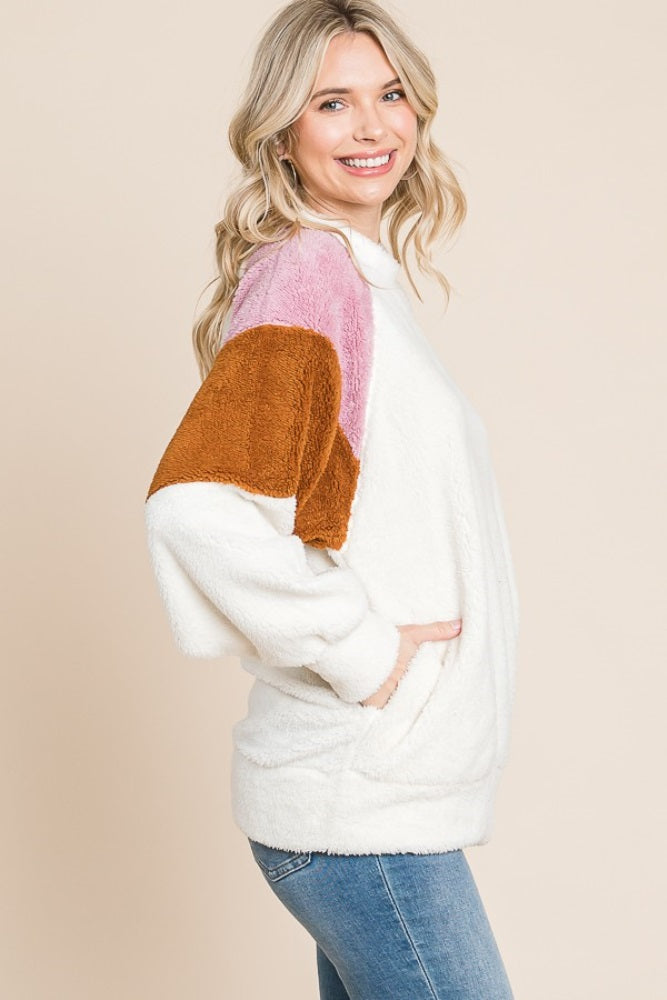 woman wearing a white fuzzy pullover sweater with brown, pink, and rust color block sleeves and side pockets