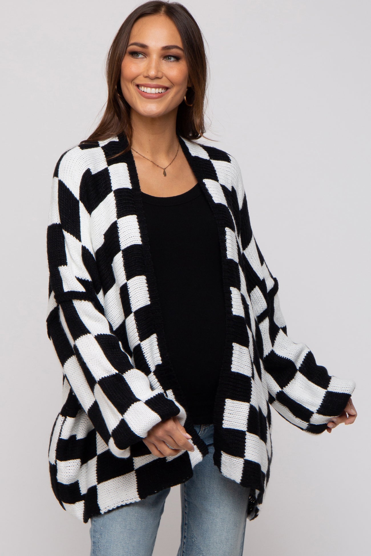 woman wearing a black and white checkered maternity cardigan over a black top and showing her baby bump