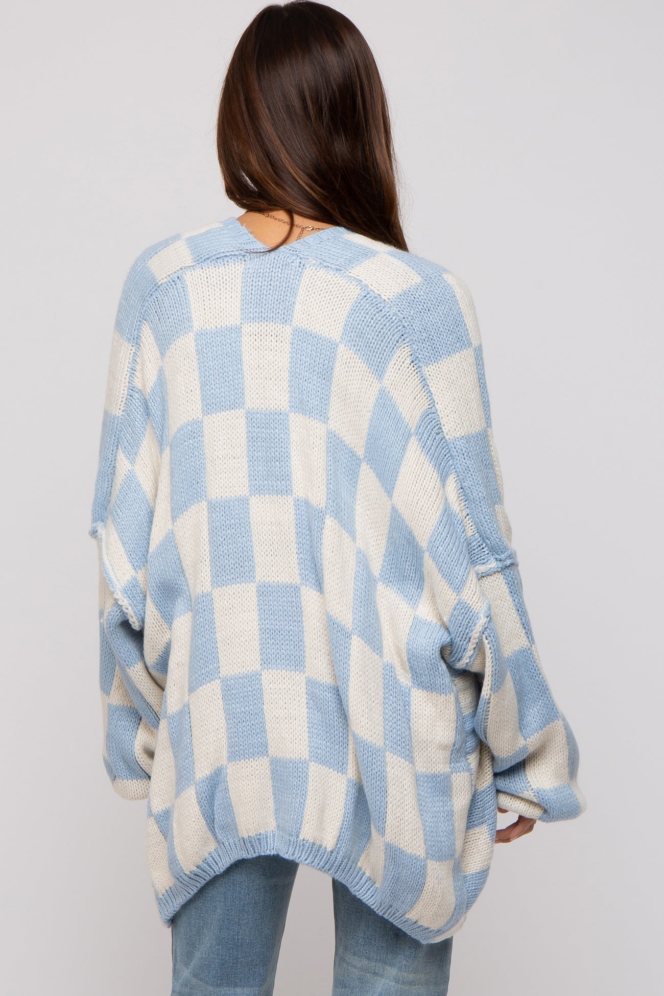 woman wearing a light blue and cream checkered oversized maternity sweater, viewed from the back