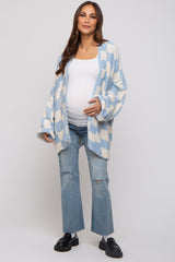 woman wearing a light blue and white checkered maternity cardigan and distressed jeans, showing her baby bump