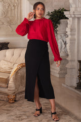 woman wearing a red pleated maternity blouse and a black ribbed maternity skirt with a side slit