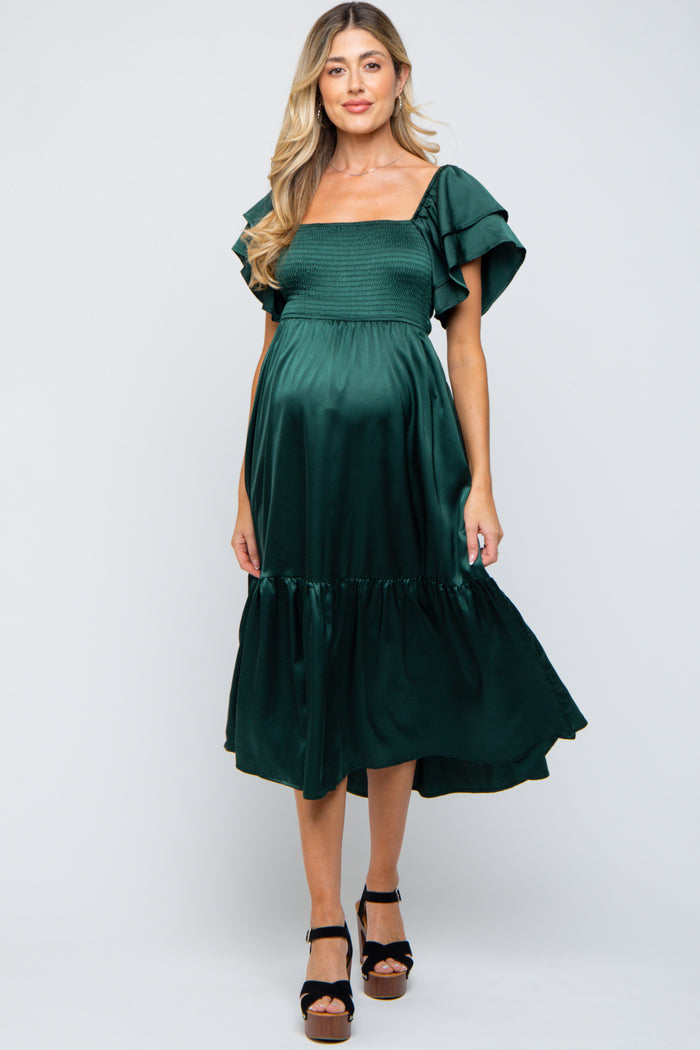 woman wearing a dark green maternity dress with flutter sleeves and a smocked bodice, showcasing her baby bump