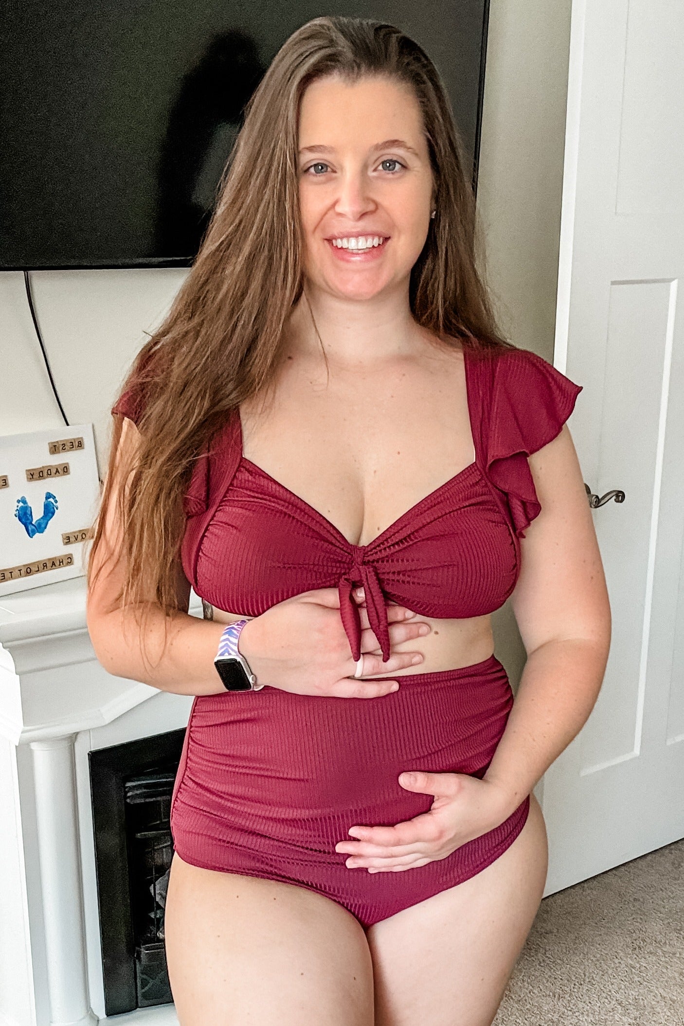 woman wearing a burgundy maternity bikini with ruffled straps and holding her baby bump