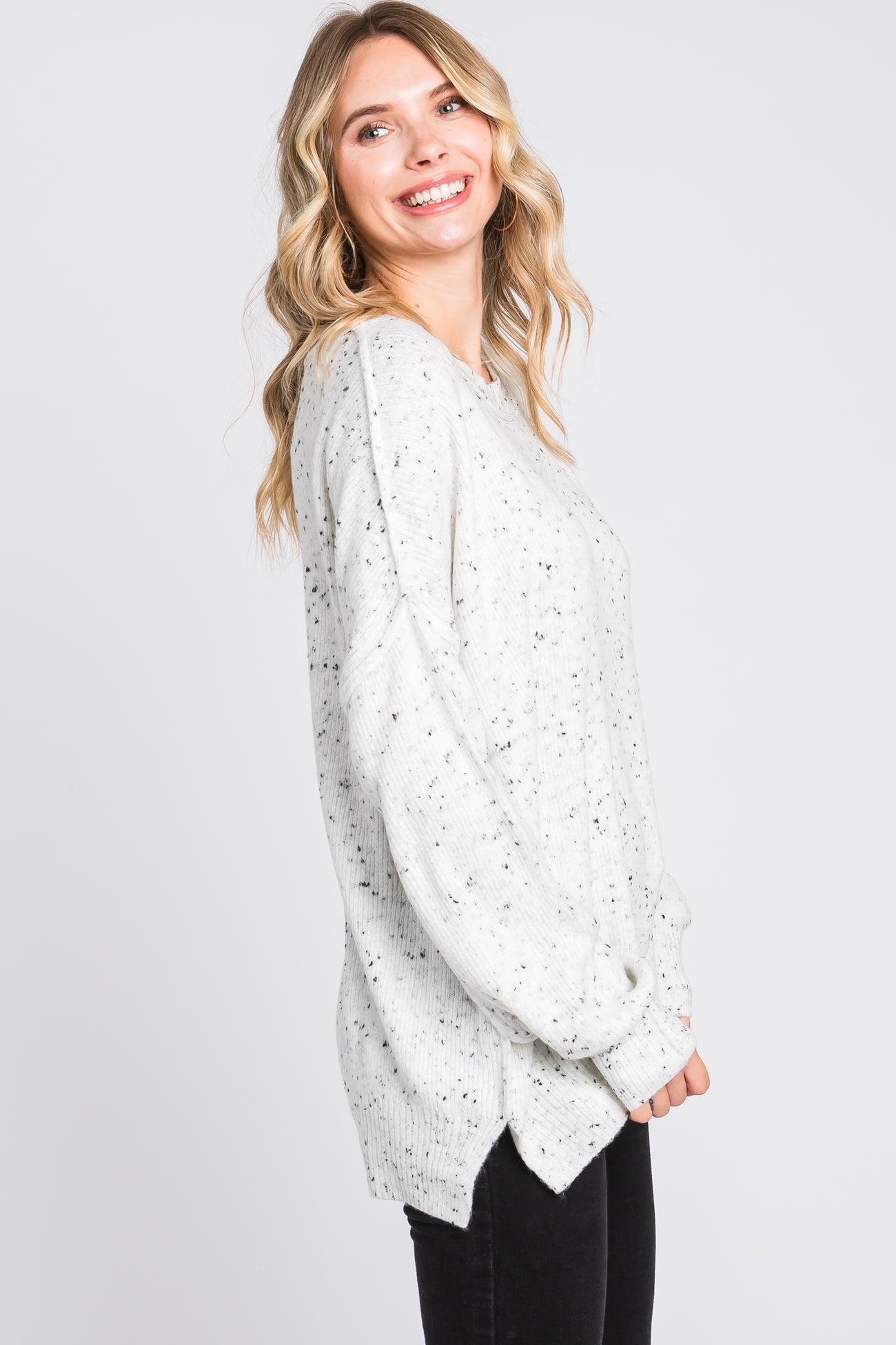 woman wearing a light gray speckled oversized sweater with a side slit, smiling and facing to the side