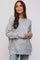 woman wearing a light gray speckled maternity sweater with a relaxed fit and side slits, holding her baby bump