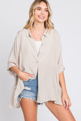woman wearing a beige and cream striped oversized button-up shirt with rolled sleeves and denim shorts