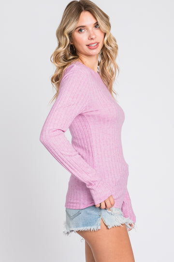 woman wearing a pink ribbed long sleeve top with a round neckline and side pockets, paired with distressed denim shorts