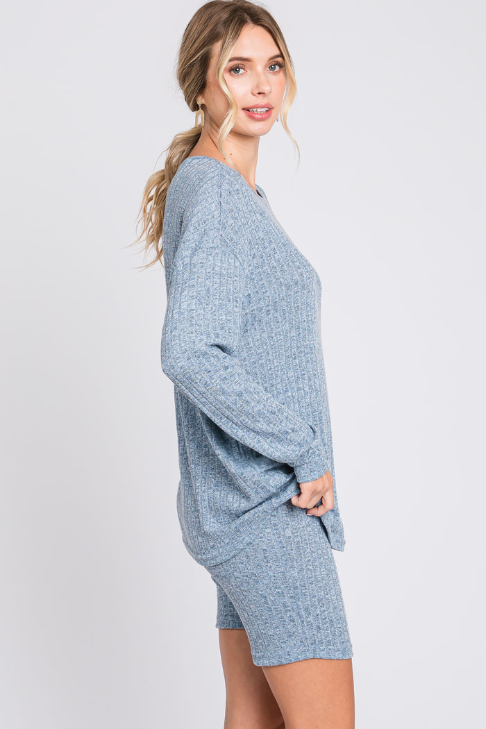 woman wearing a light blue ribbed sweater and matching shorts, posing sideways against a plain background