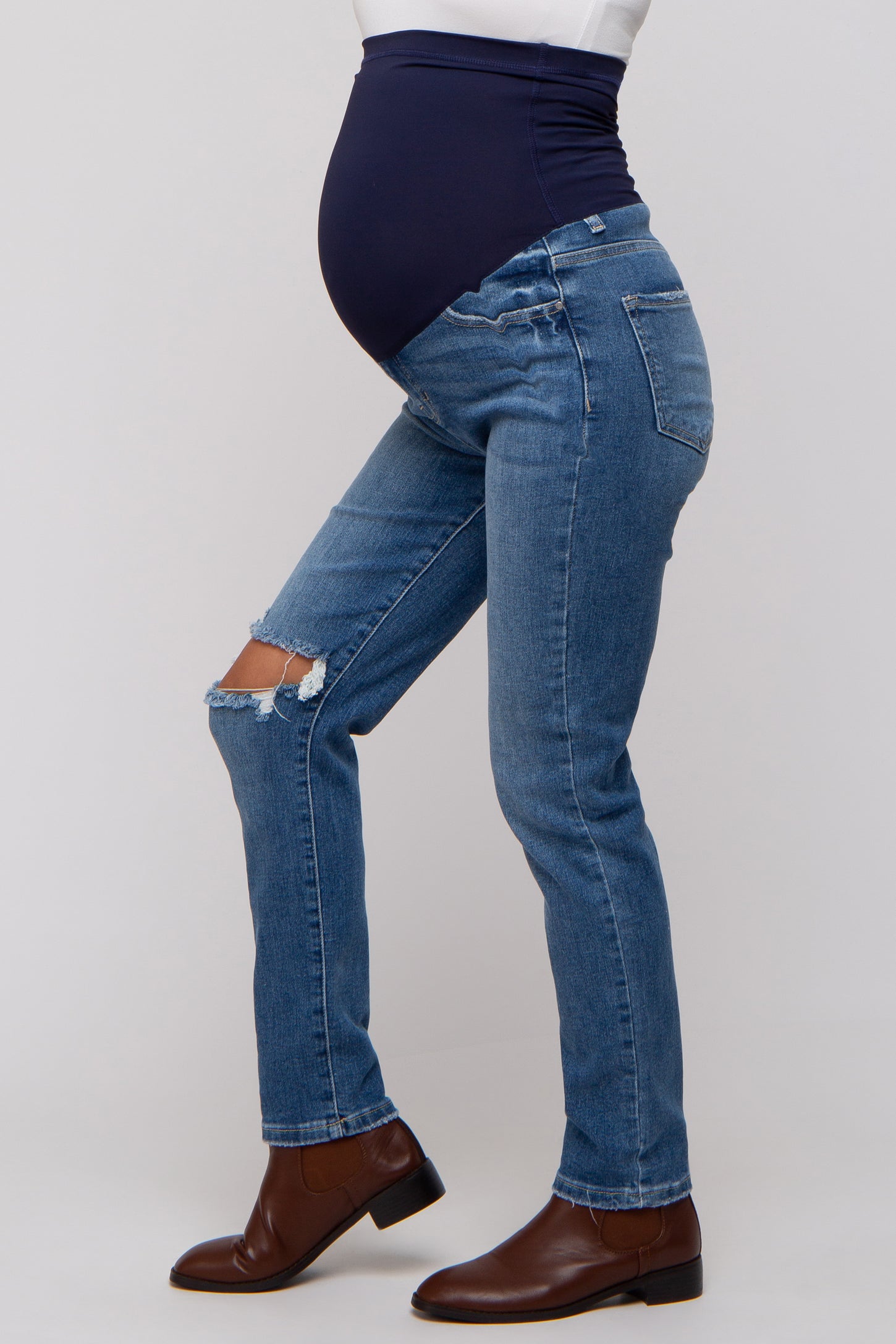 woman wearing blue distressed maternity jeans with a dark blue belly support band and showcasing a baby bump