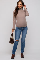 woman wearing a tan ribbed maternity top and blue distressed jeans, showing her baby bump and holding a brown handbag