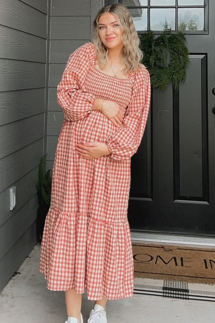 woman wearing a red and white gingham maternity dress with puff sleeves and tiered skirt, gently holding her baby bump