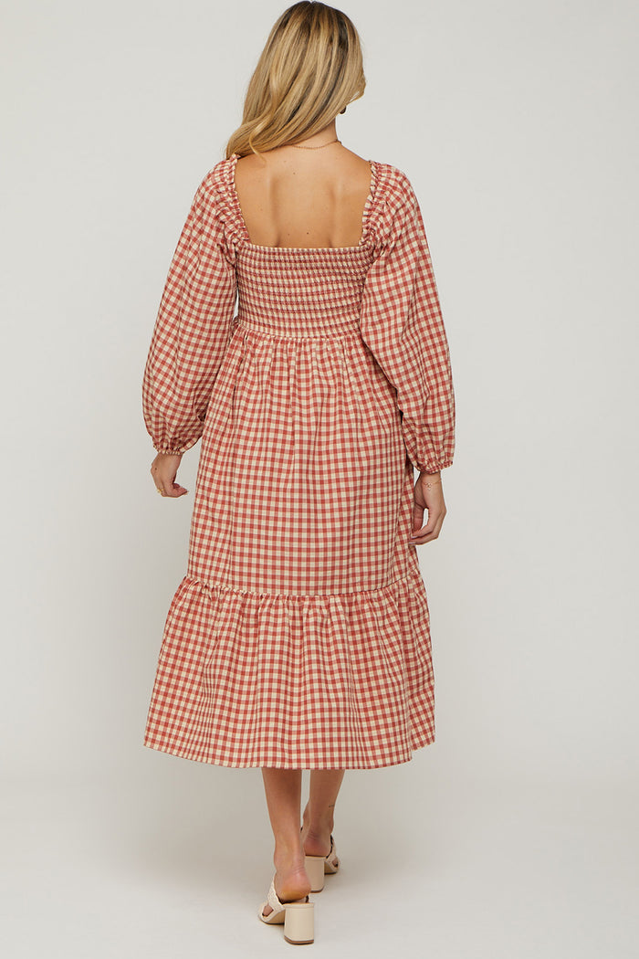 woman wearing a pink and white gingham maternity dress with puff sleeves and a tiered skirt, showing her baby bump