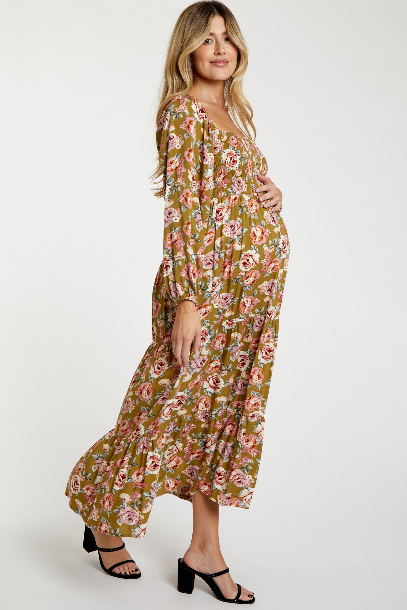 woman wearing a floral maternity maxi dress in green and pink, showing her baby bump while standing sideways