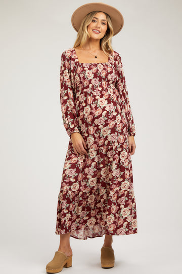 woman wearing a burgundy floral maternity dress with long sleeves and a ruffled skirt, showcasing her baby bump