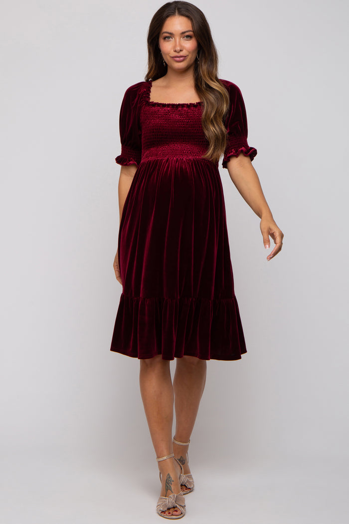 woman wearing a burgundy maternity dress with a smocked bodice and short puff sleeves, featuring a ruffle hem
