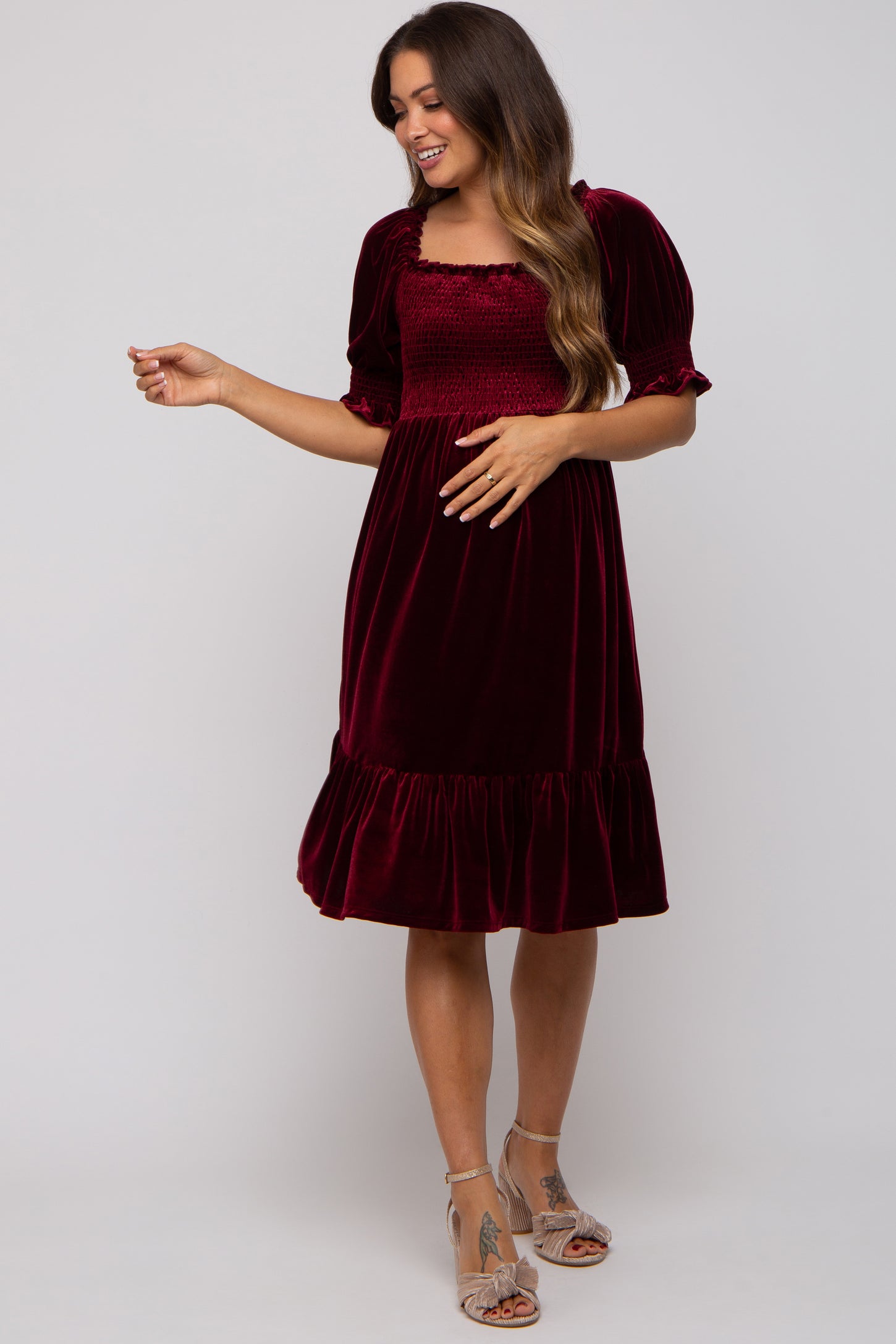 woman wearing a burgundy velvet maternity dress with puff sleeves and a ruffled hem, showing her baby bump
