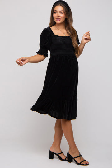 woman wearing a black velvet maternity dress with short puff sleeves and a ruffled hem, showcasing her baby bump