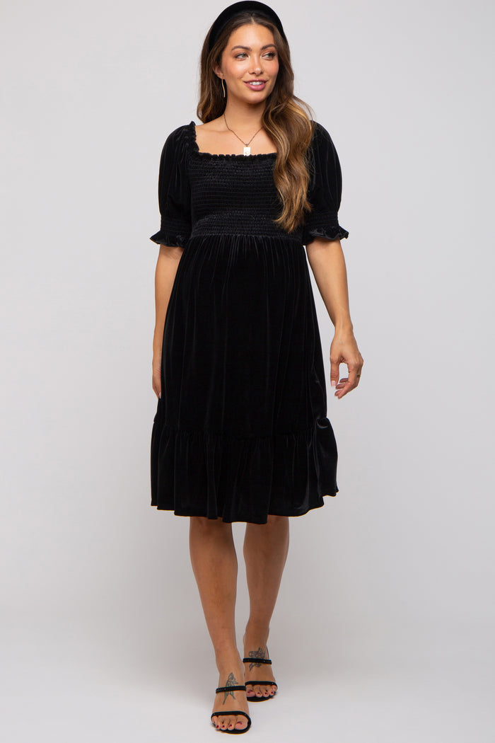woman wearing a black velvet maternity dress with short puff sleeves and a ruffled hem, showing a baby bump