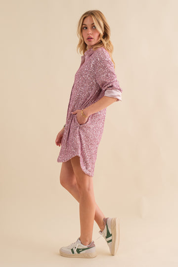woman wearing a pink sequin shirt dress with rolled sleeves and pockets, styled with white sneakers