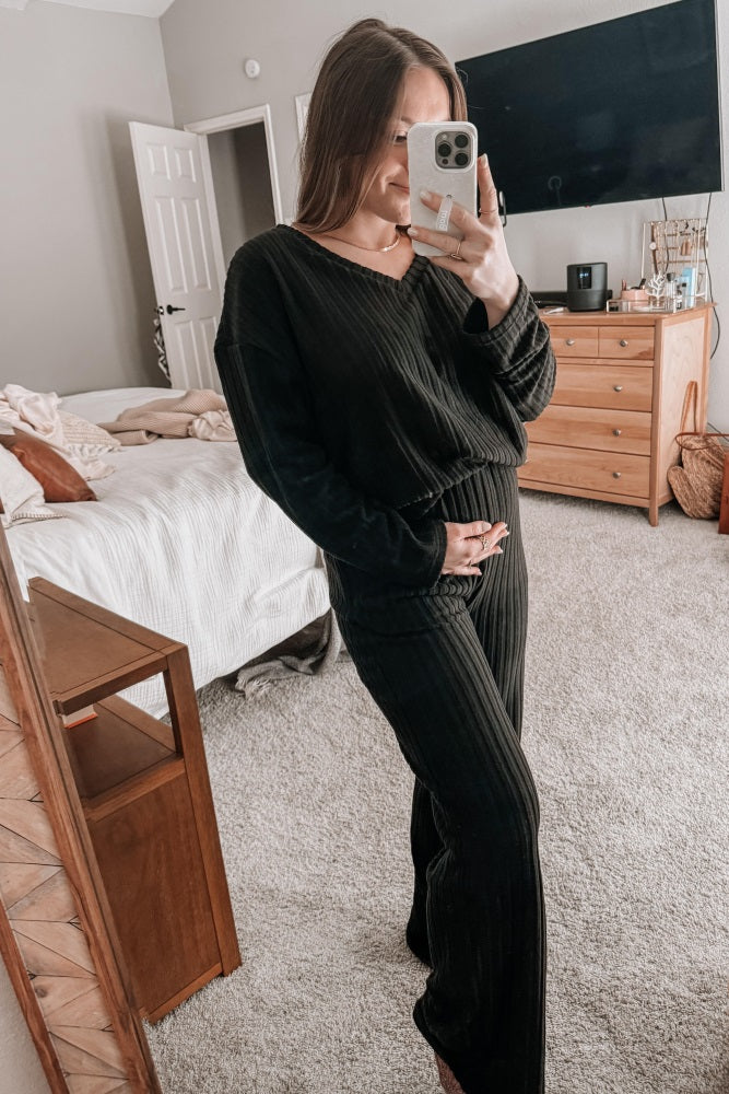 woman wearing a black ribbed maternity loungewear set and gently holding her baby bump