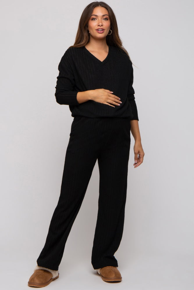 woman wearing a black maternity loungewear set with a v-neck top and wide-leg pants, holding her baby bump