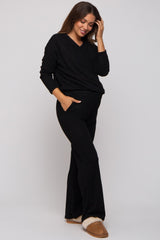 woman wearing a black maternity loungewear set with a v-neck sweater and wide-leg pants, holding her hair.