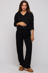 woman wearing a black v-neck maternity sweater and black ribbed maternity pants, holding her baby bump