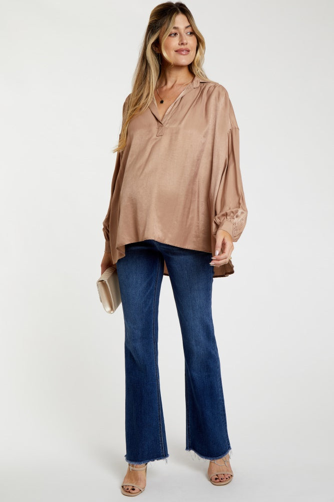 woman wearing a brown maternity top with a v-neck and billowy sleeves, paired with flared jeans and heels, holding a clutch