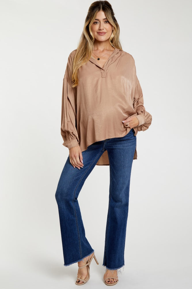 woman wearing a beige maternity top with a v-neck and billowing sleeves styled with flared jeans and heels.