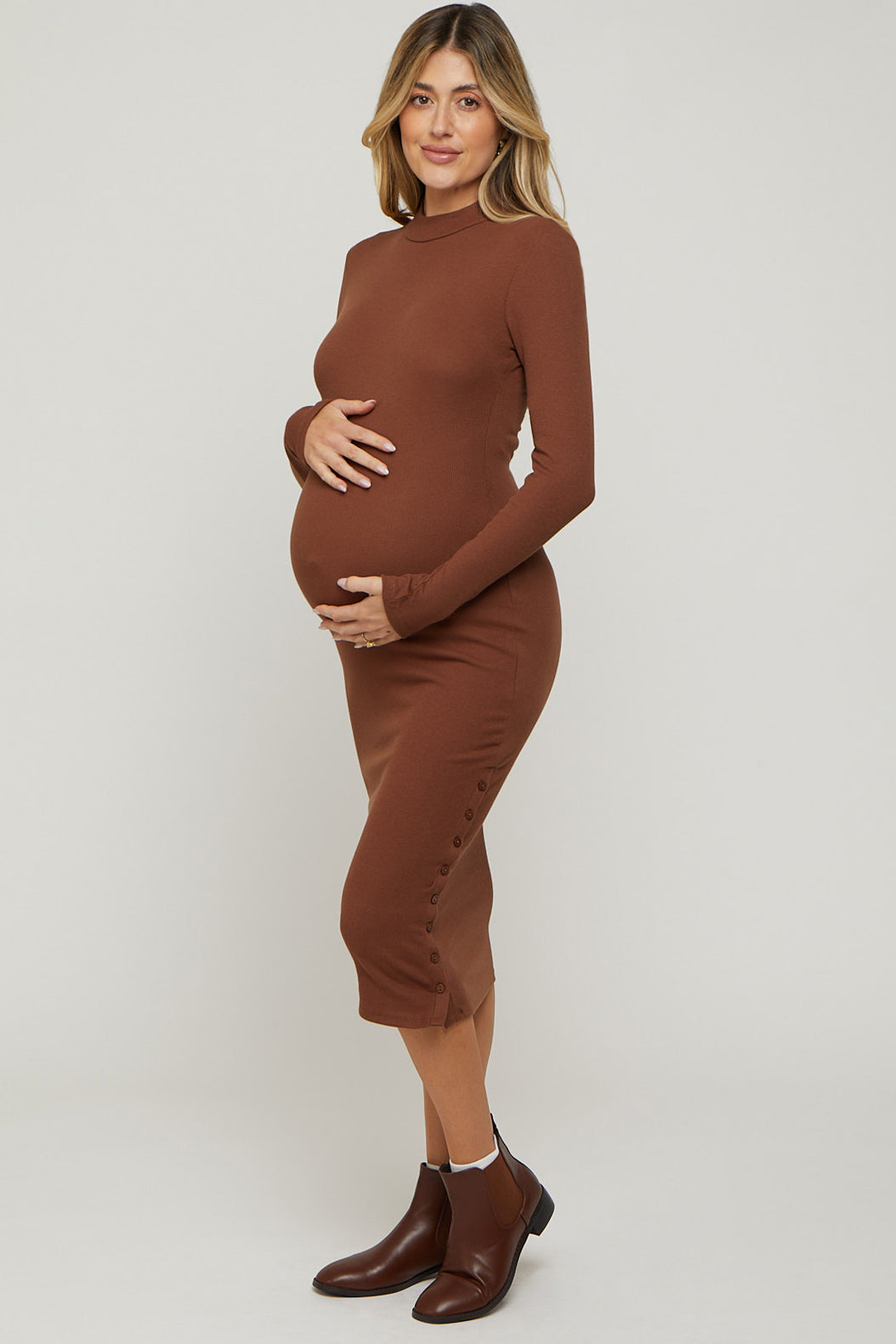 woman wearing a brown long sleeve maternity dress with button details and holding her baby bump