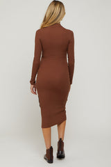 woman wearing a brown long sleeve ribbed maternity dress with a side slit, showing her back and styled with ankle boots