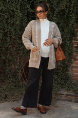 woman wearing a beige knitted maternity cardigan over a white top and black wide-leg pants, holding a brown bag and showing her baby bump