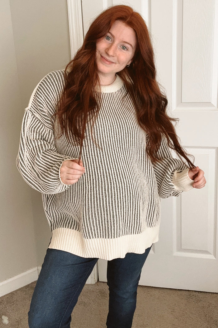 woman wearing a striped maternity sweater in gray and cream, showcasing her baby bump with a smile