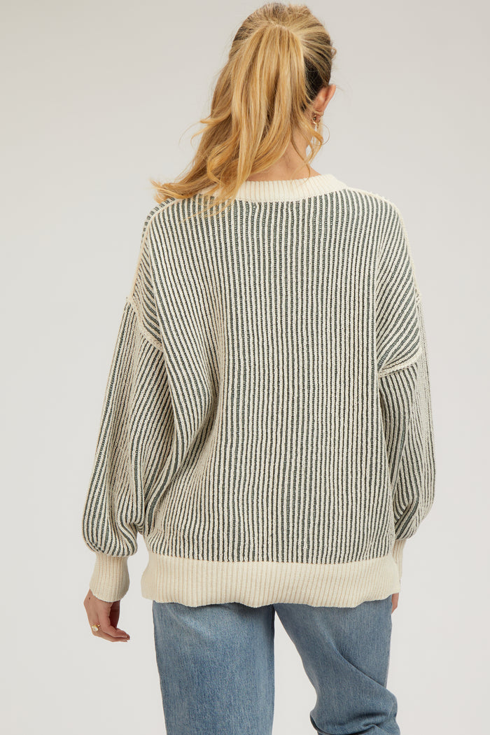 woman wearing a striped light beige and gray oversized maternity sweater, viewed from the back