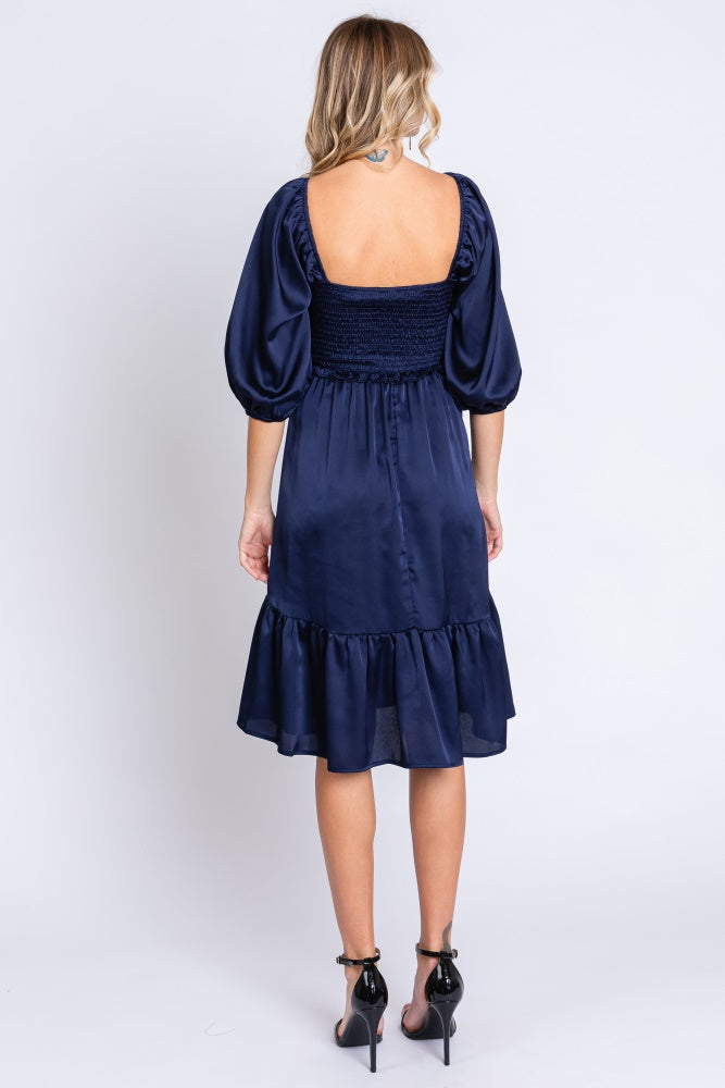 woman wearing a navy blue puff sleeve dress with a smocked bodice and ruffle hem.