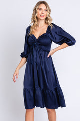 woman wearing a navy blue satin dress with a smocked bodice and puff sleeves, featuring a ruffled hemline