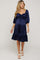 woman wearing a navy blue maternity dress with puff sleeves and a tiered ruffled hem, showing her baby bump