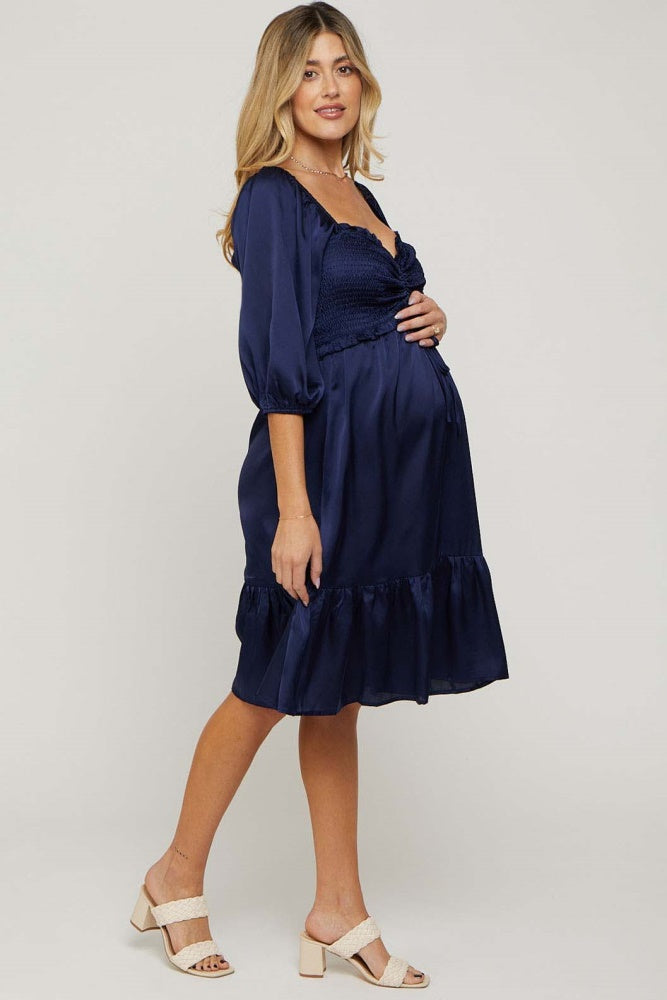 woman wearing a navy blue maternity dress with a smocked bodice and ruffled hem, holding her baby bump