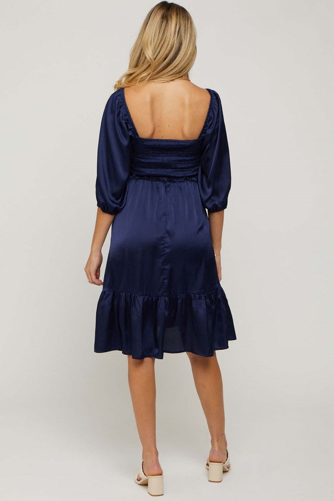 woman wearing a navy blue satin maternity dress with a smocked back and puff sleeves, showing her back
