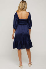 woman wearing a navy blue satin maternity dress with a smocked back and puff sleeves, showing her back