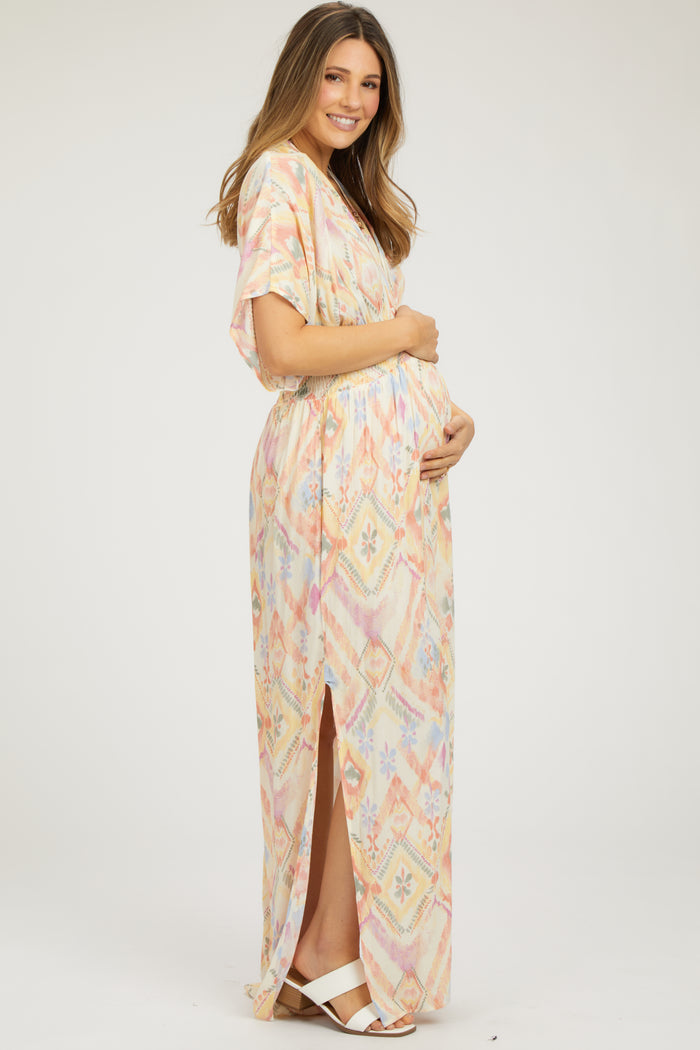 woman wearing a colorful patterned maternity maxi dress with a side slit, holding her baby bump